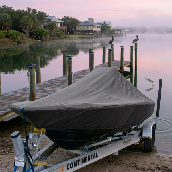 Covered boat on a Continental trailer at a wooden dock, calm water reflecting a pink dawn sky with houses in the background.
