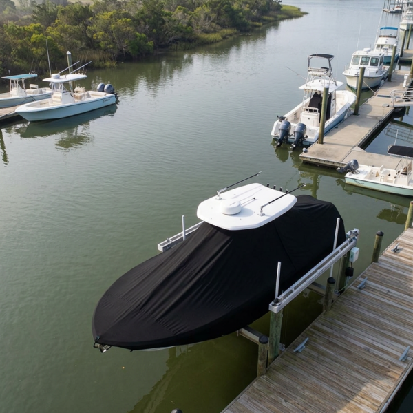 A large boat covered with a black tarp sits on a wooden dock in a marina, with calm water and several other boats nearby.