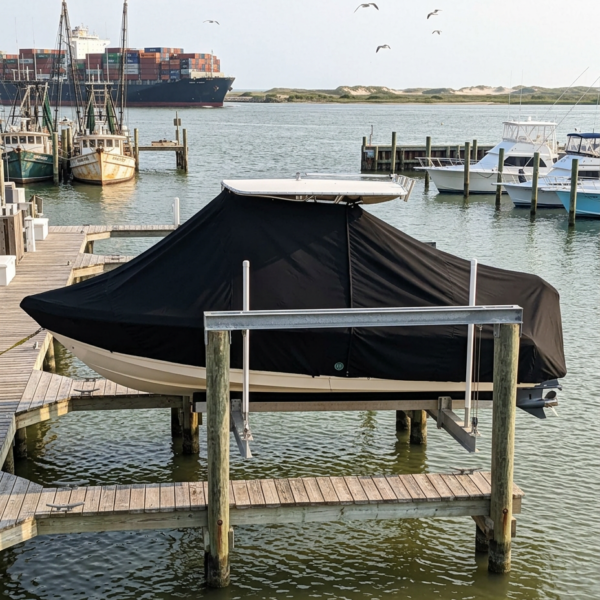 Covered motorboat on a docked lift at a marina, with calm water and other boats in the background.