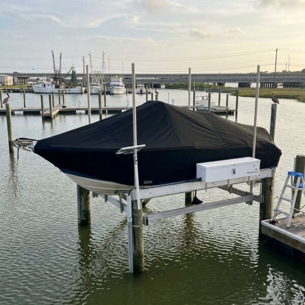 Boat on a lift at a marina, covered with a black tarp and calm water around it.