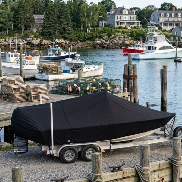 Boat on a trailer with a black cover at a harbor dock, nearby lobster pots and moored boats with houses in the background.