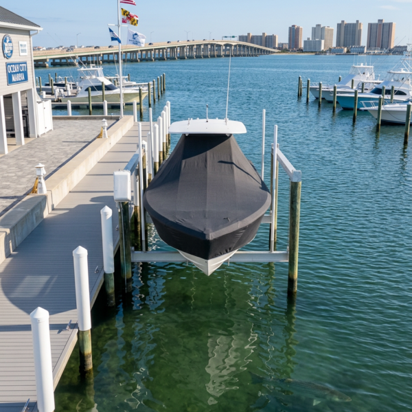 Covered boat on a lift at a marina, with docks, flags, and a distant city skyline over calm green water.