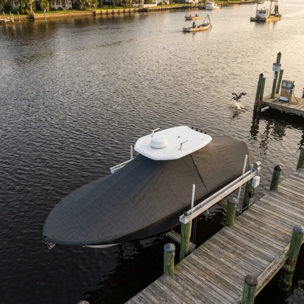 Covered motorboat with a white radar dome moored at a wooden dock along a calm river, with house-lined shoreline in the background.