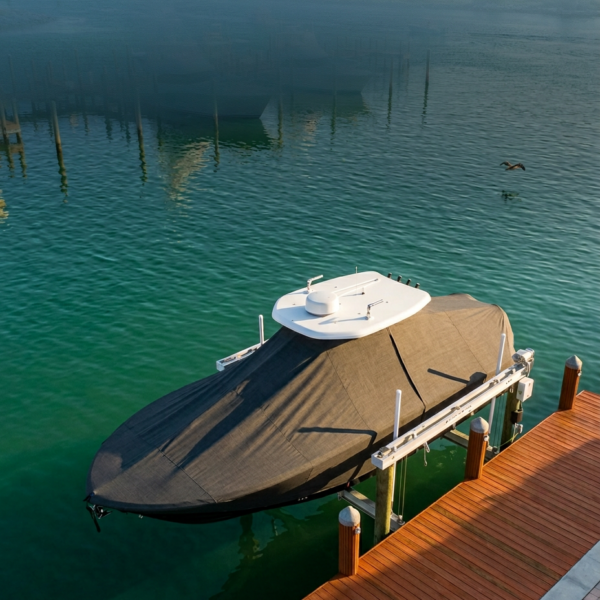 Motorboat covered with a dark tarp docked at a wooden pier on turquoise water, with a white radar arch on its deck.