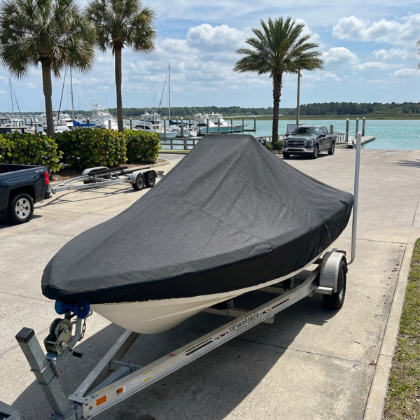 Boat on a trailer covered with a black tarp at a marina, palm trees and blue water in the background.