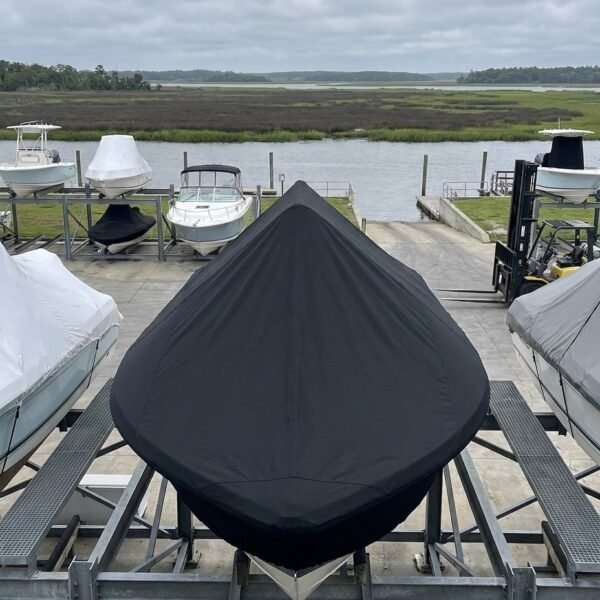 Center boat covered with a black cover on a metal cradle at a marina, with water and marsh beyond.