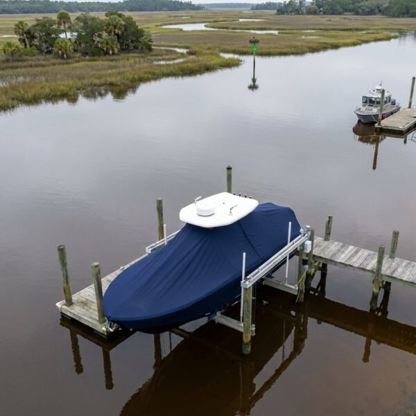 Covered blue boat on a wooden dock extending into a calm marsh channel; another small boat seen in the distance under gray skies