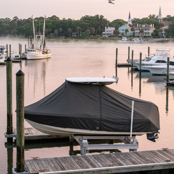 Covered motorboat on a lift at a wooden marina pier at dawn with pastel sky and calm water