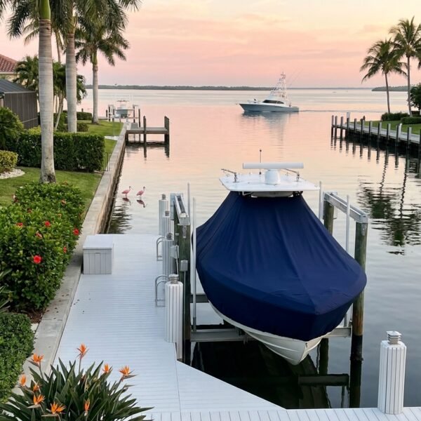 Covered boat docked at a white pier beside palm trees at sunset with calm water.