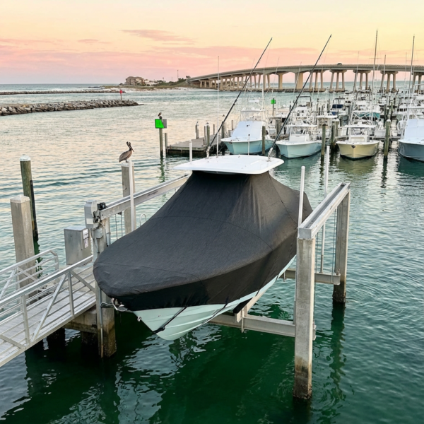 Covered motorboat on a lift at a marina during sunset, with calm water and other boats in the background.