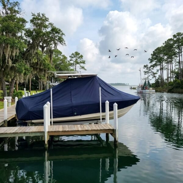 Boat covered with a navy tarp docked at a wooden pier, calm water reflecting sky and trees.