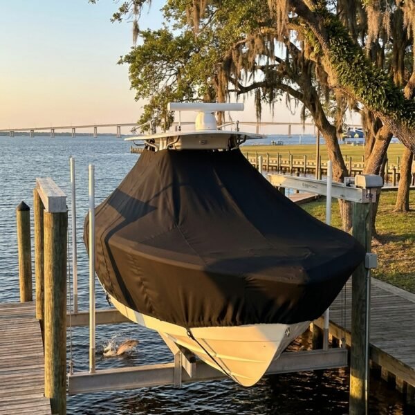 Boat on a lift dock, covered with a black canvas, by calm water at sunset.