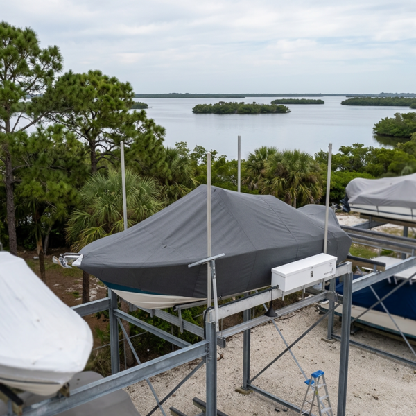 Boat on a metal boat lift covered with a gray tarp, overlooking a waterway with trees in the background.