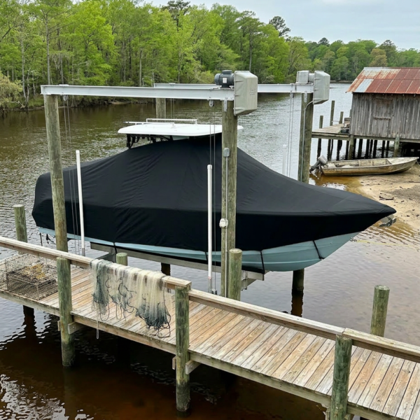 Boat in a covered tarp docked at a wooden pier beside calm water, with a shed in the background and green trees beyond.