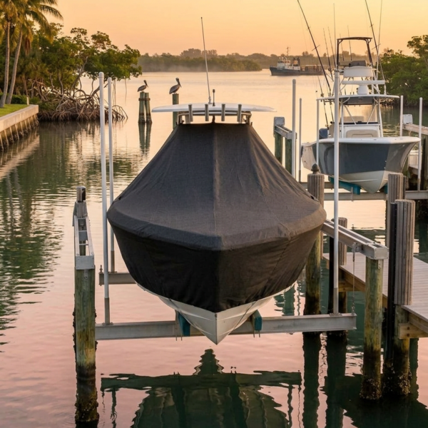 A black-covered boat on a lift at a marina during sunset, with palm trees and calm water in the scene.