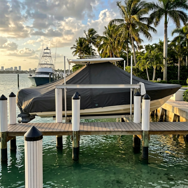Boat covered with a gray tarp on a wooden dock by turquoise water, palm trees and a sunset sky in the background.