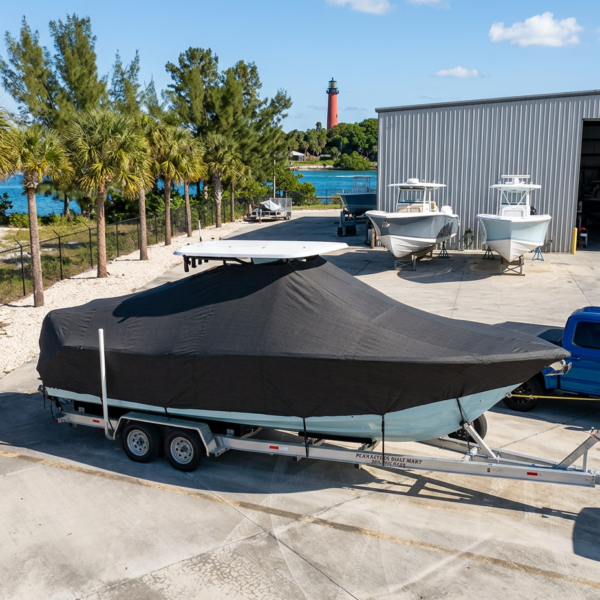 Covered boat on a trailer at a marina with palm trees and a lighthouse in the distance.