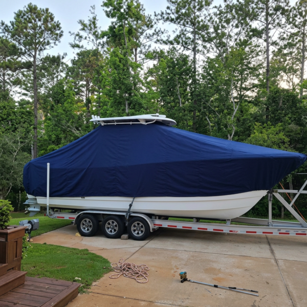Blue-covered boat on a triple-axle trailer in a driveway with trees in background, ready for storage or transport.