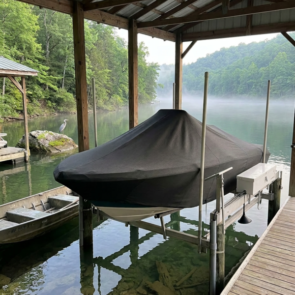 Covered boat on a lift under a wooden boathouse overlooking a misty green lake with forested hills in the background.