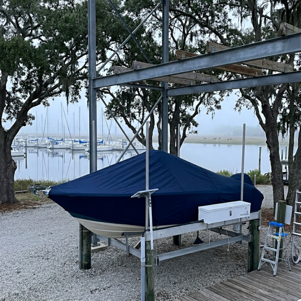 Blue-covered boat on a lift by a marina, with a white cooler attached and a small ladder nearby on the dock.