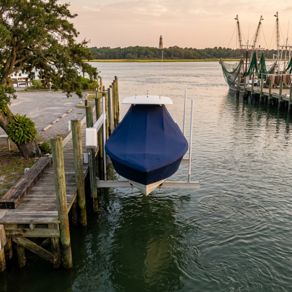 Blue boat on a lift at a quiet marina, with water, a dock, and a distant lighthouse at sunset