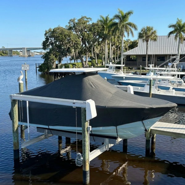 Covered motorboat on a lift at a marina with palm trees and calm water in the background