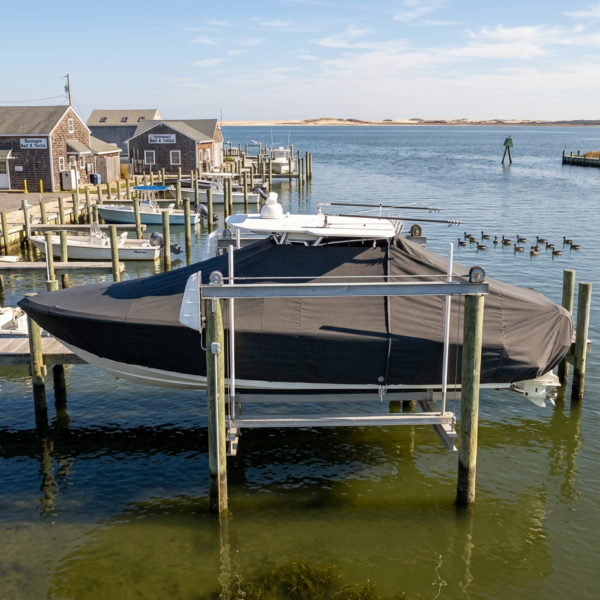 Covered motorboat docked at a wooden pier in a calm harbor with houses and boats in the background, and ducks on the water nearby