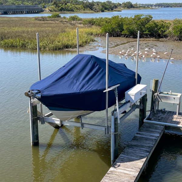 Blue-covered boat on a lift at a wooden dock beside a marsh, with pink flamingos in the background.
