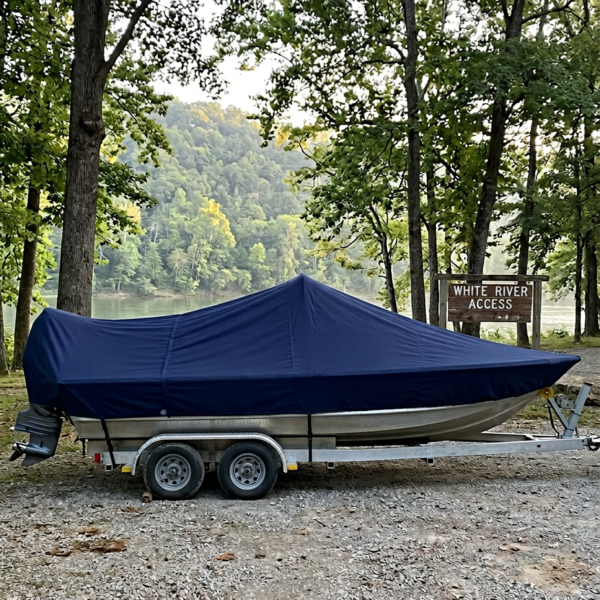 Blue boat covered with tarp on a trailer beside a wooded lakefront at White River Access site.