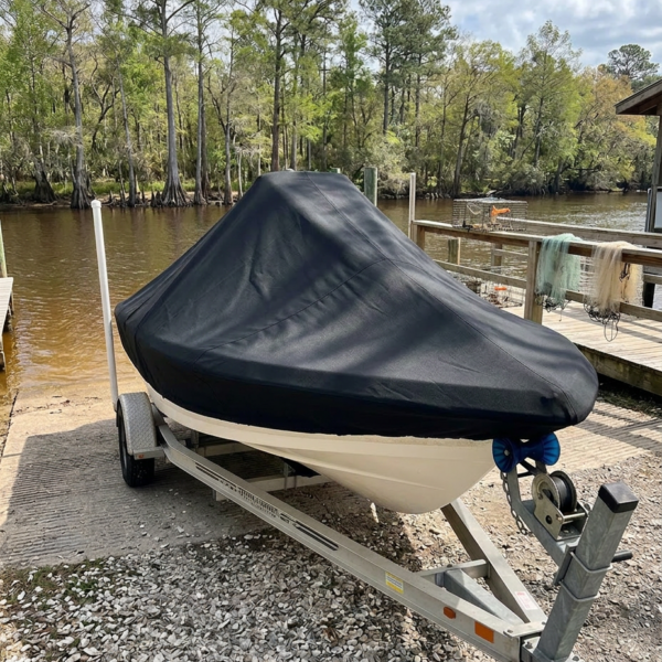 White boat on a trailer, covered with a black tarp, parked by a lake with a wooden dock.