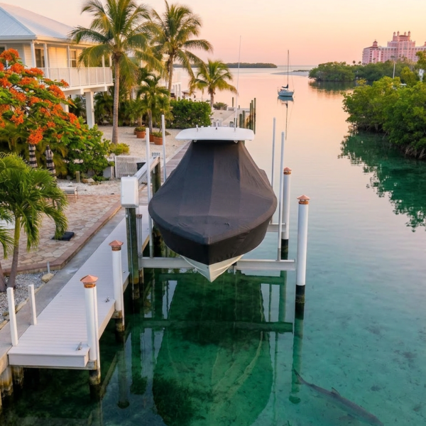 A shaded canal-side scene with a covered boat on a lift in clear turquoise water, palm trees, and pastel sunset sky.