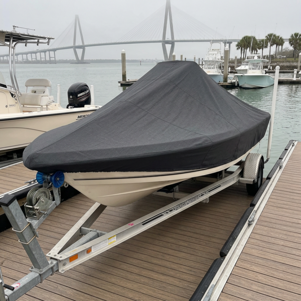 Boat on a trailer docked at a marina, covered with a dark tarp, with a bridge in the foggy background and other boats nearby