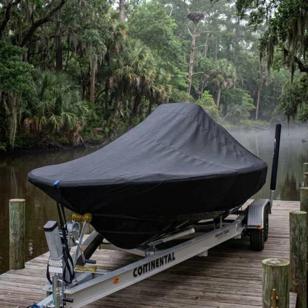 Covered speedboat on a trailer parked on a wooden dock by a misty lake and dense trees in the background