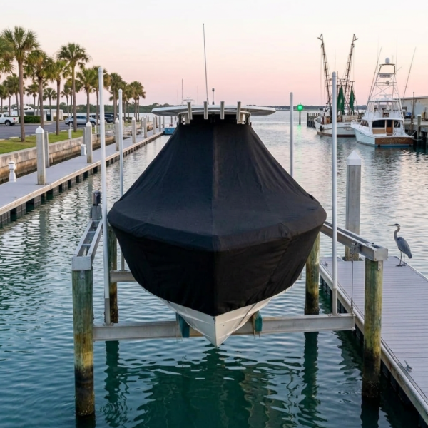 Covered speedboat on a lift at a marina with palm trees and a pastel sunset. The water is calm and turquoise-colored.