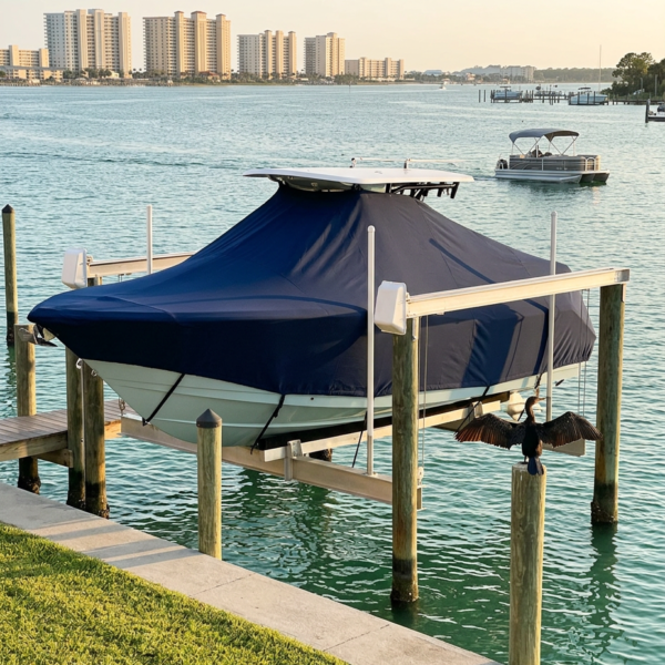 Covered powerboat on a lift at a marina with calm turquoise water and a distant city skyline.