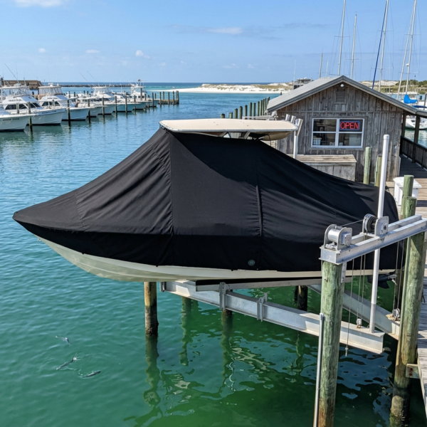 A boat docked at a marina with a black cover over the hull and a small shed in the background.